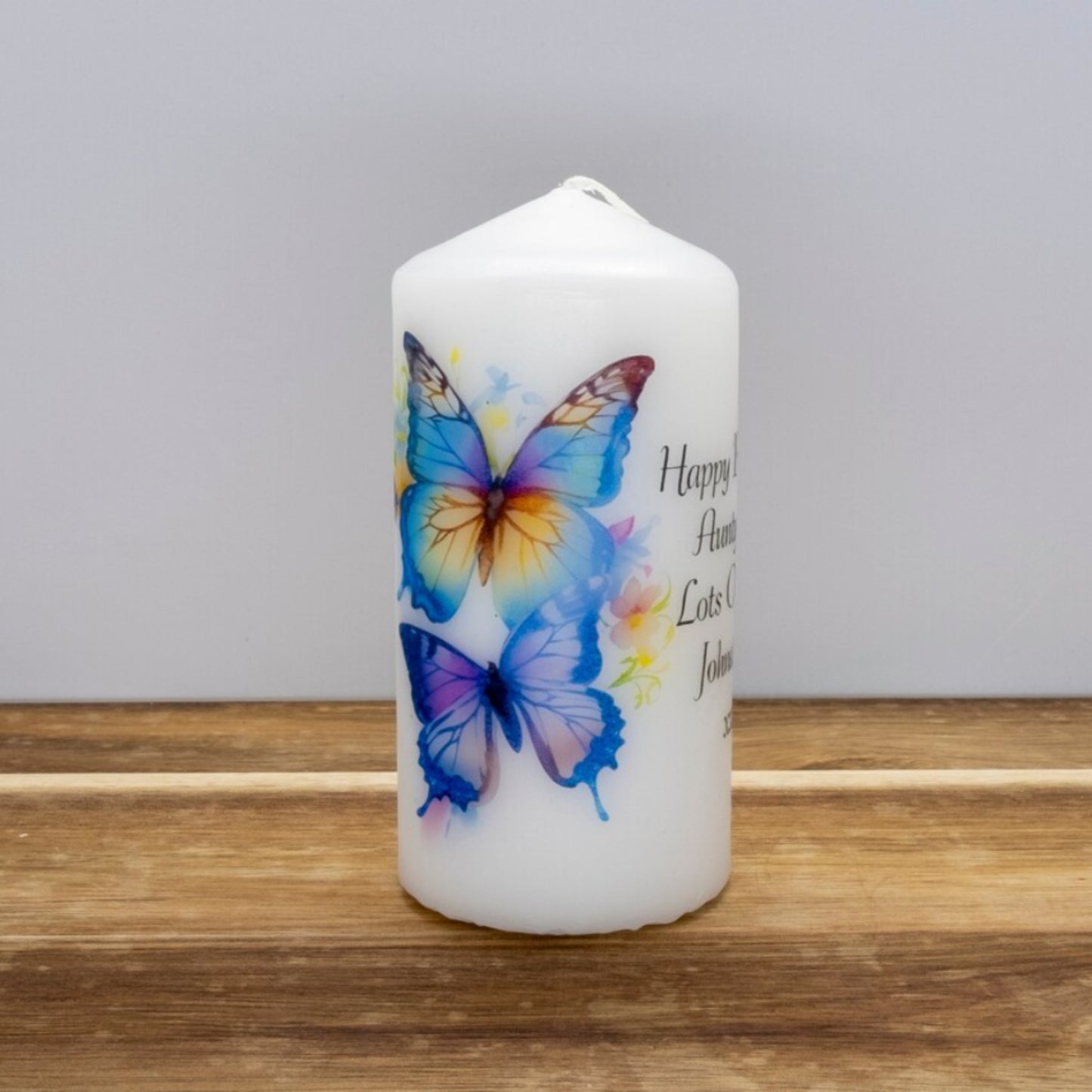 A set of four personalized birthday candles with a butterfly design, each in different sizes, displayed on a wooden surface.