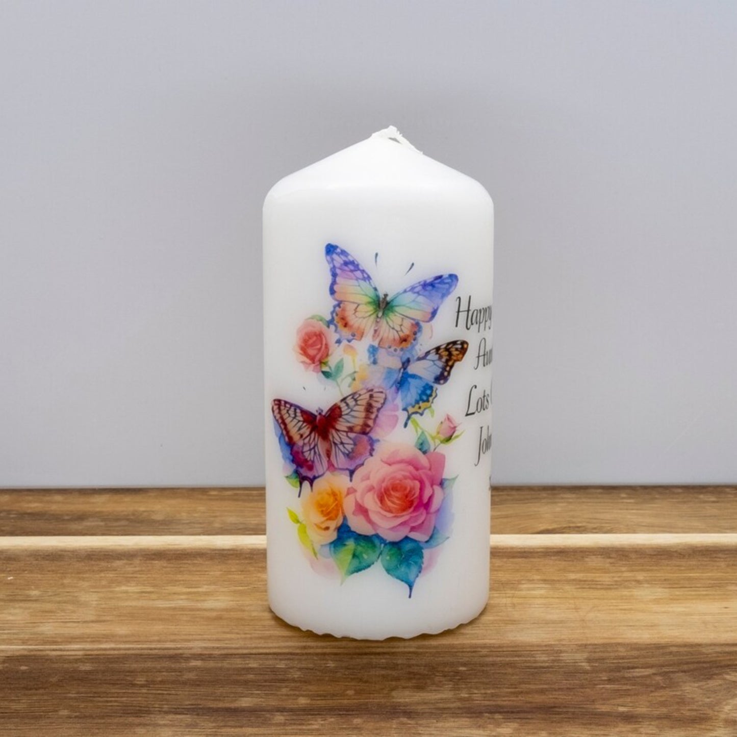 A set of four personalized birthday candles with a butterfly design, each in different sizes, displayed on a wooden surface.