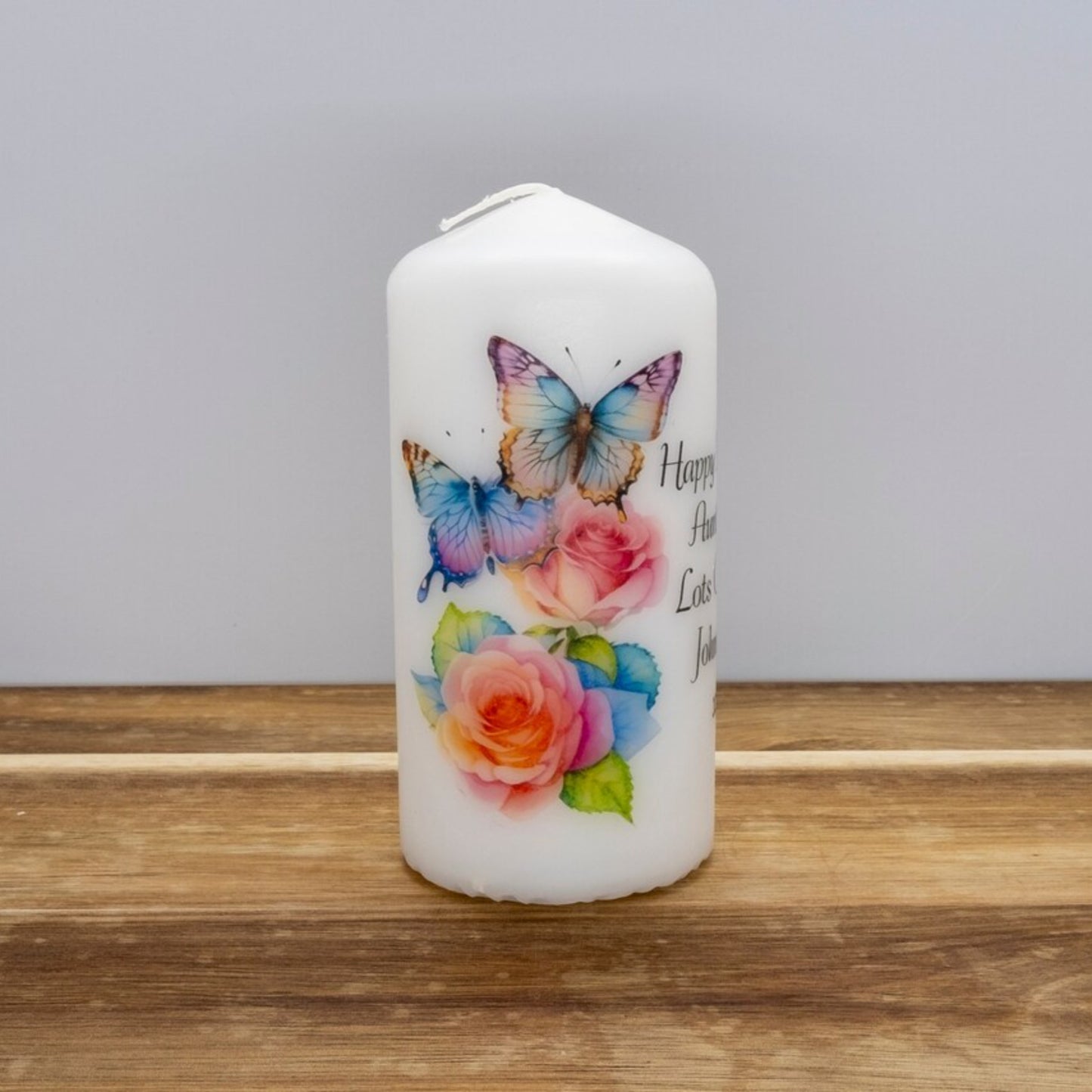 A set of four personalized birthday candles with a butterfly design, each in different sizes, displayed on a wooden surface.