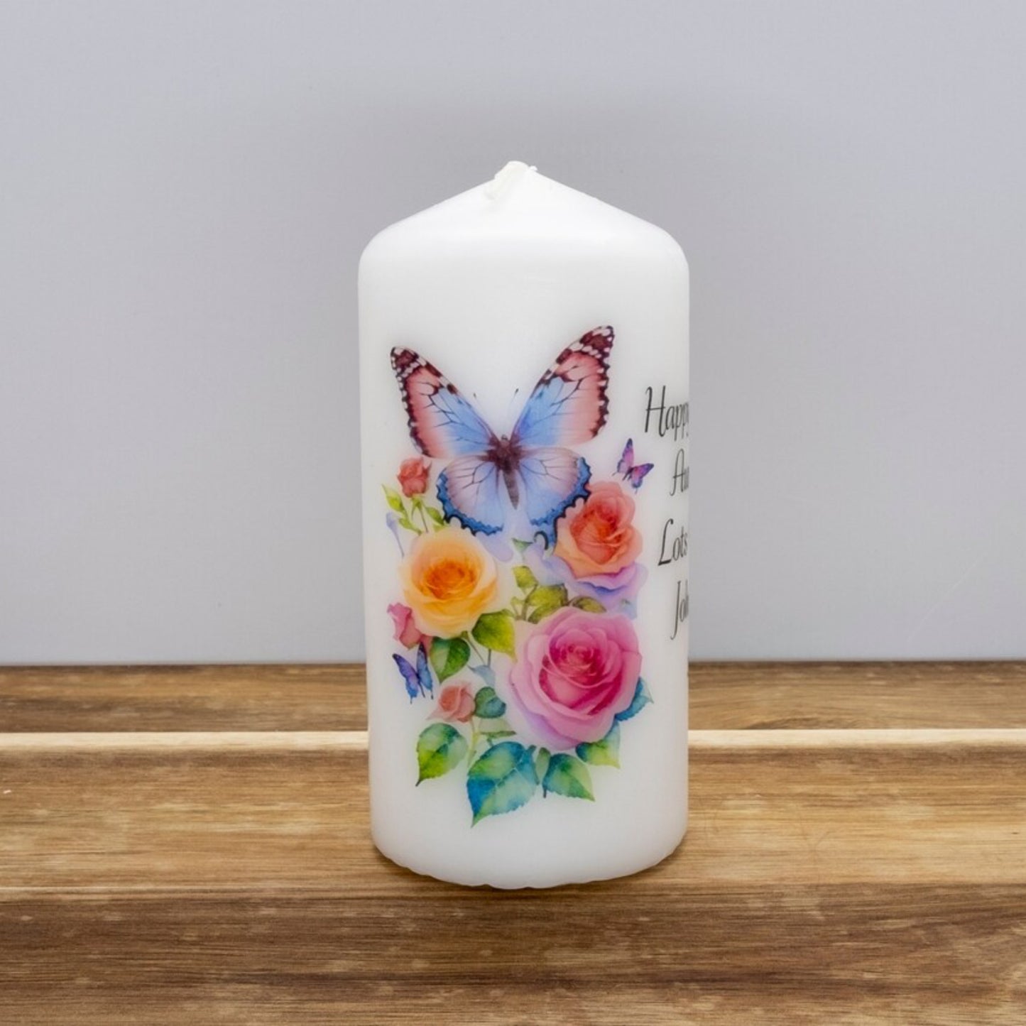 A set of four personalized birthday candles with a butterfly design, each in different sizes, displayed on a wooden surface.