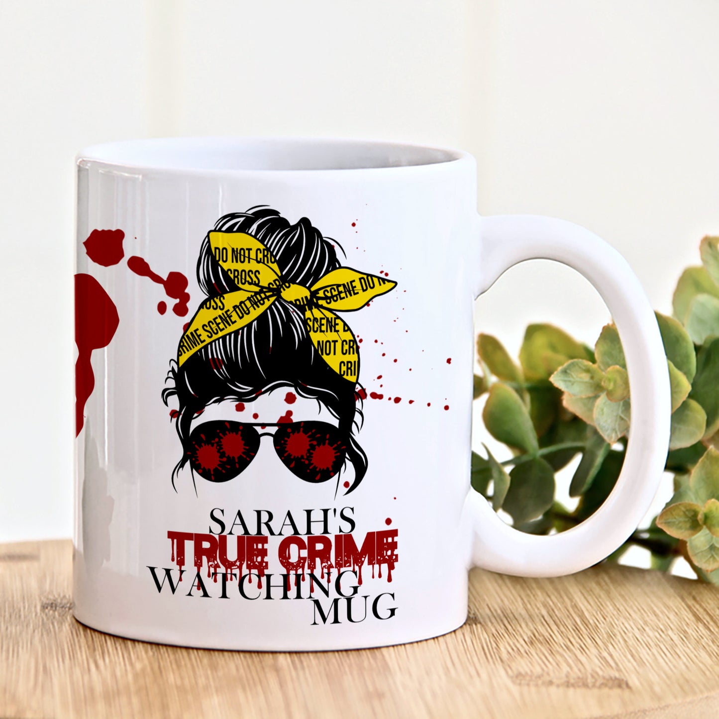 A white ceramic mug with a print of a messy bun character styled as a detective, surrounded by blood splatters, and the text 'This is my true crime watching mug or coaster'.