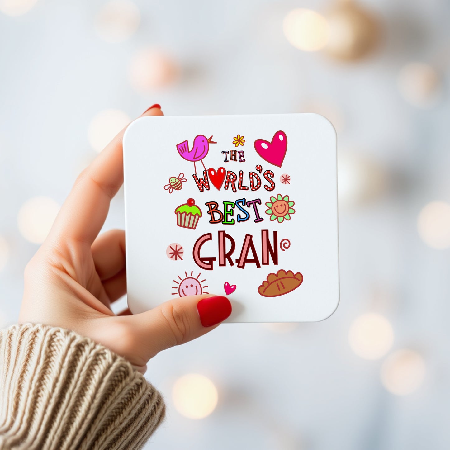 Hand holding a card with 'The World's Best Gran' text and illustrations on a blurred background