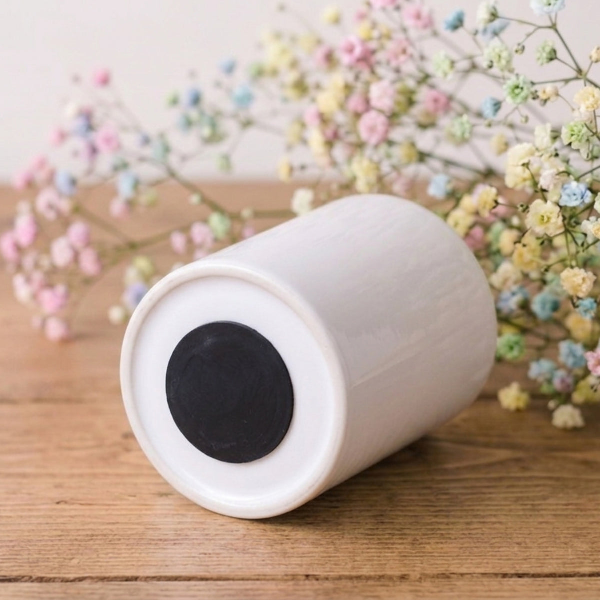 White cylindrical object with black center on a wooden surface with flowers in the background