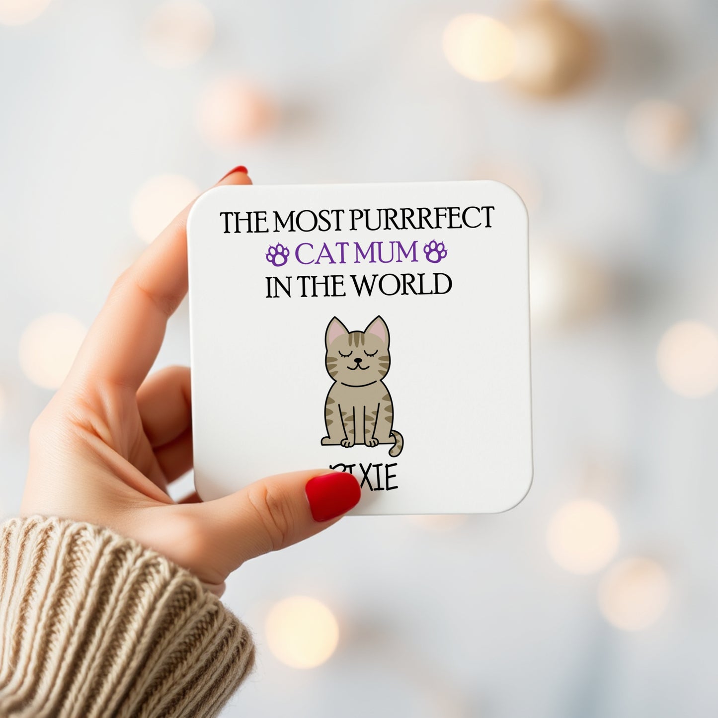 Coaster with a cat illustration and text held by a hand against a blurred light background