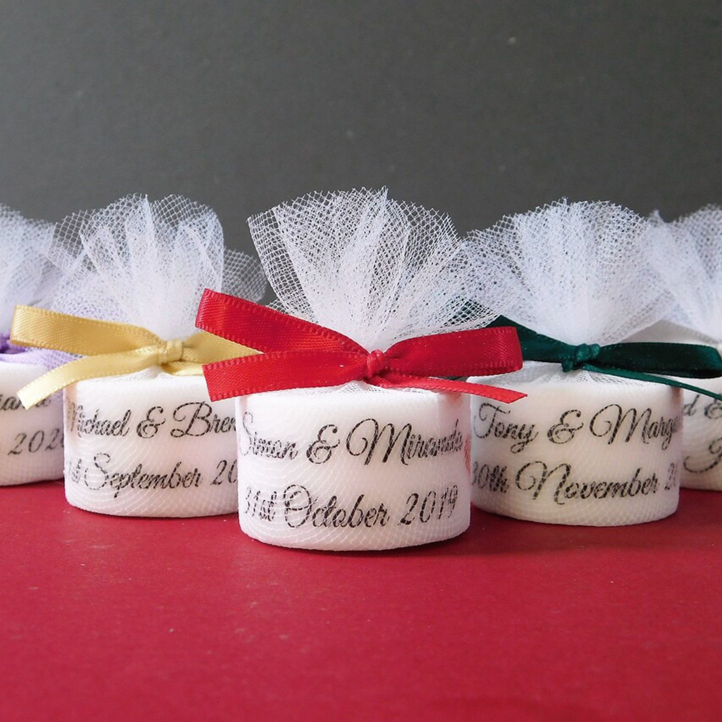 Decorative candles with personalised inscriptions and ribbons on a red surface.