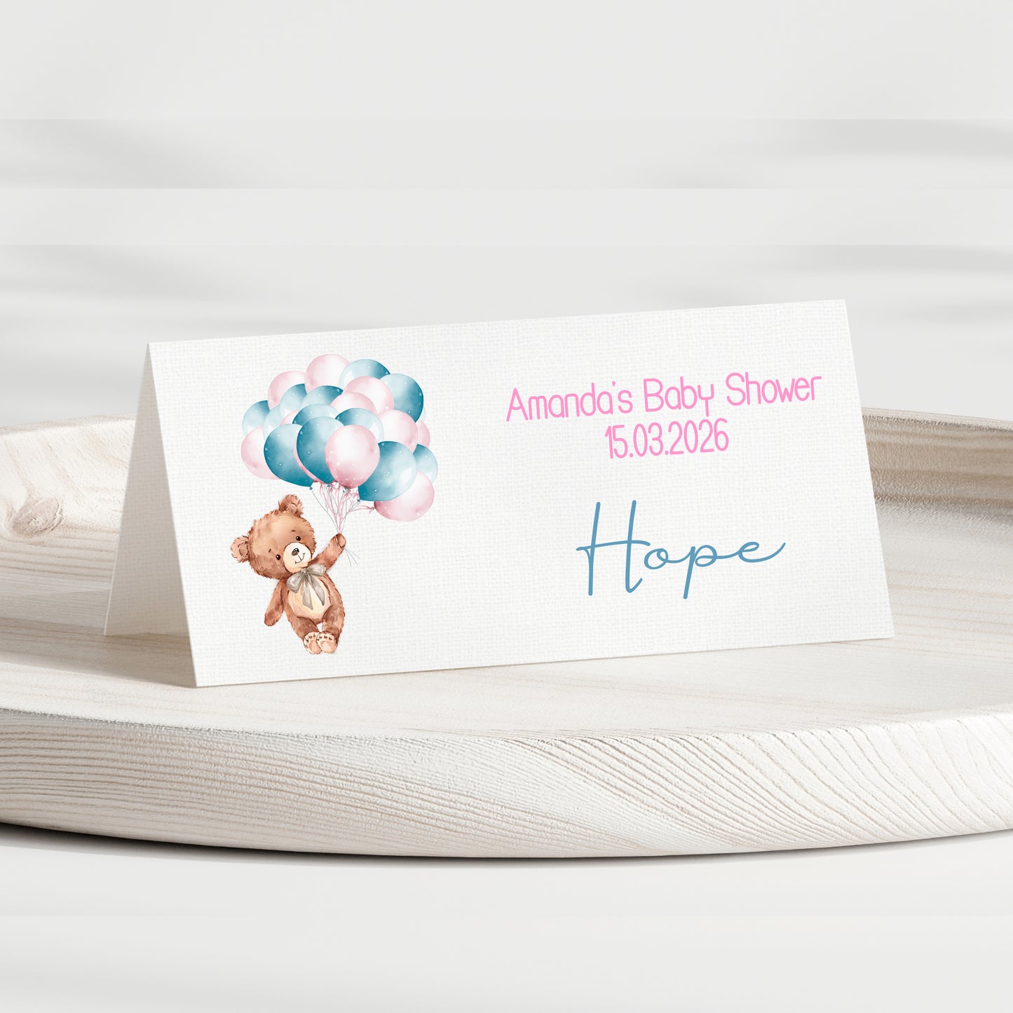 Baby shower invitation card with teddy bear and balloons on a white surface