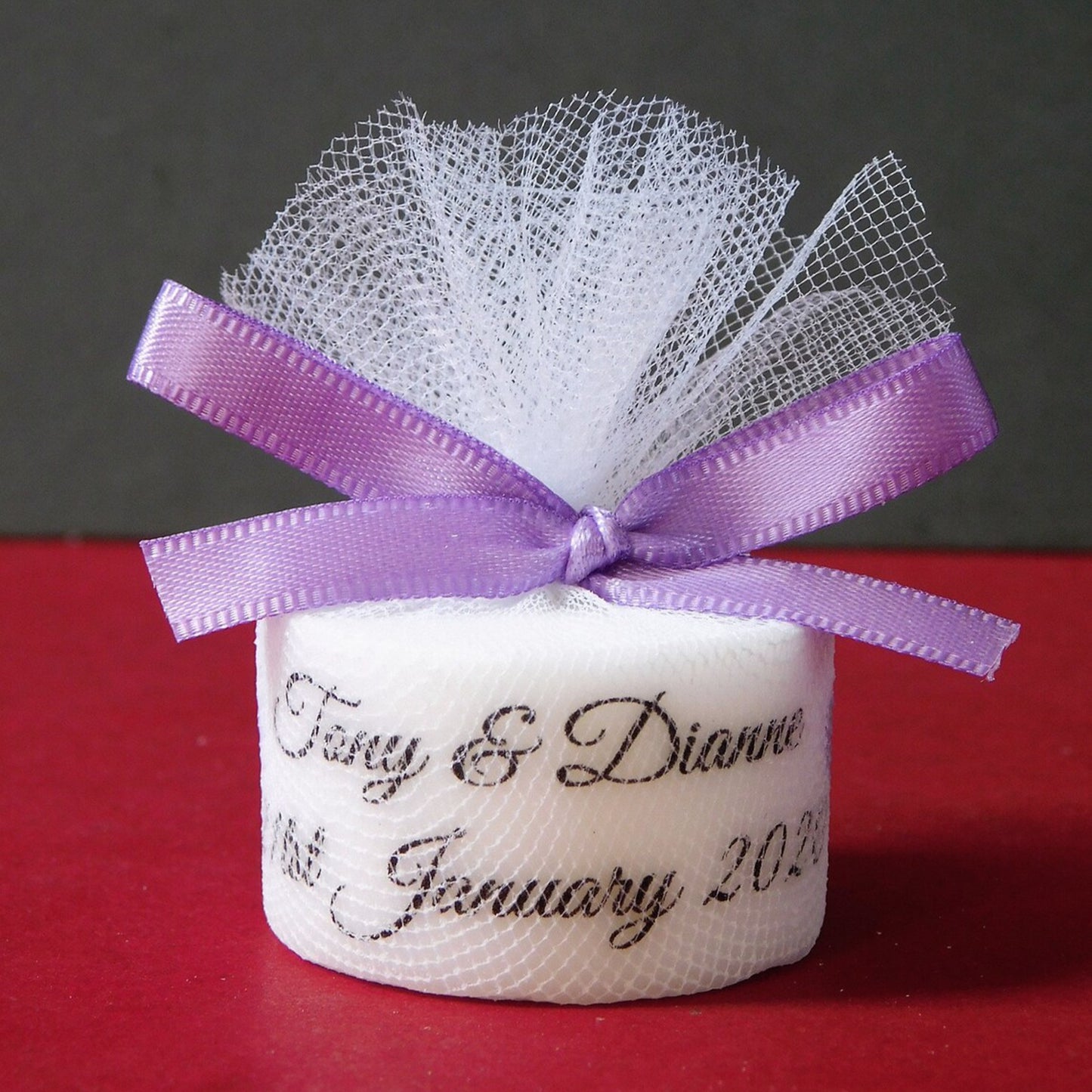 Small white candles with a purple ribbon and personalised text on a red surface