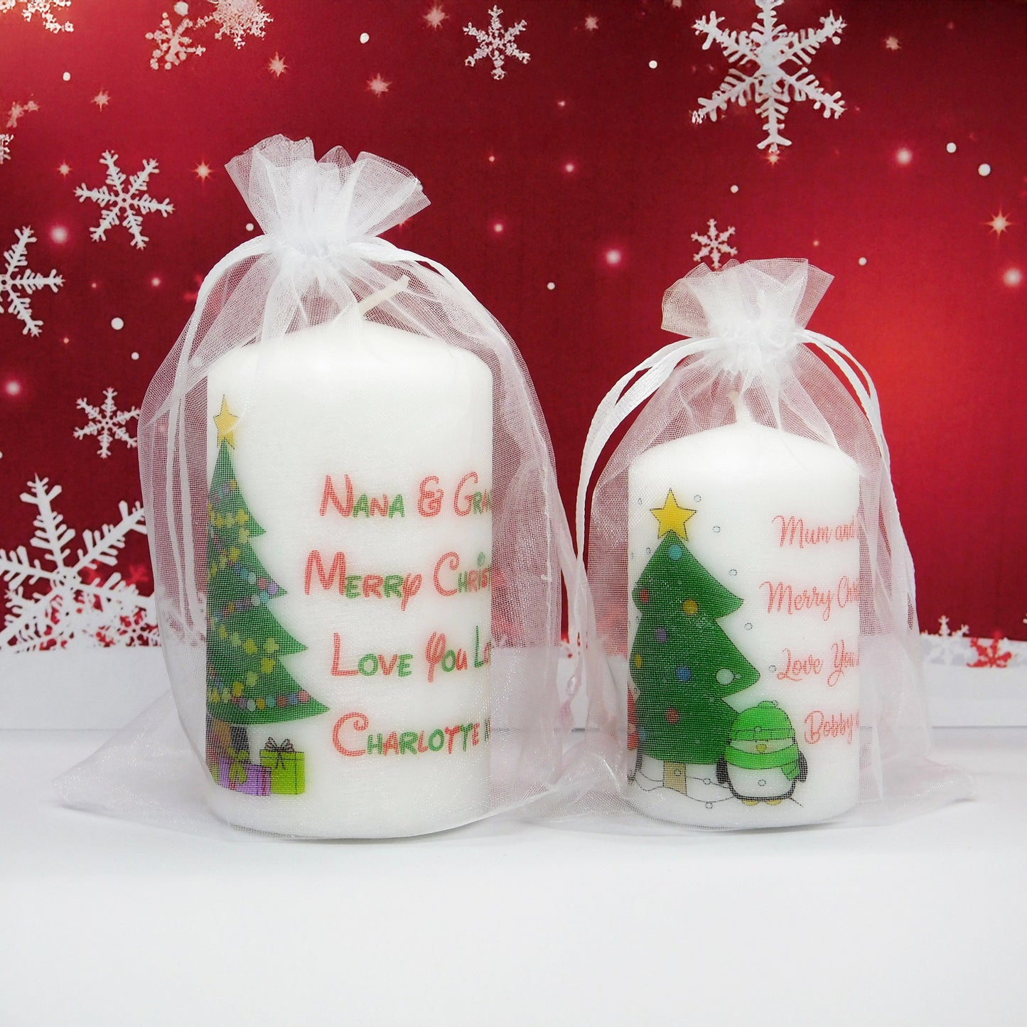 Two Christmas-themed candles in sheer bags with personalized text on a red background with snowflakes.