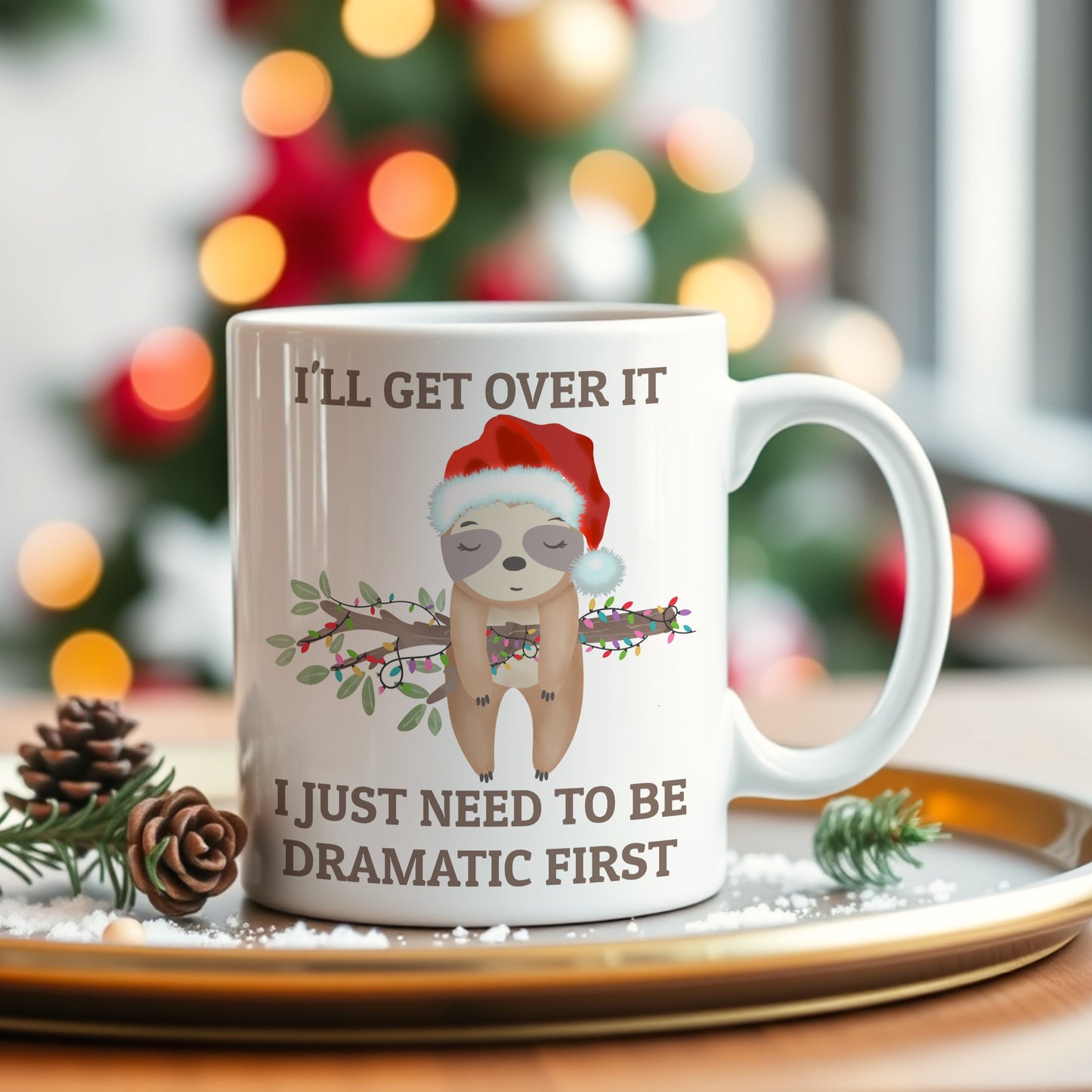 White mug with a sloth wearing a Santa hat and Christmas-themed text, placed on a decorative tray with a blurred Christmas tree in the background.