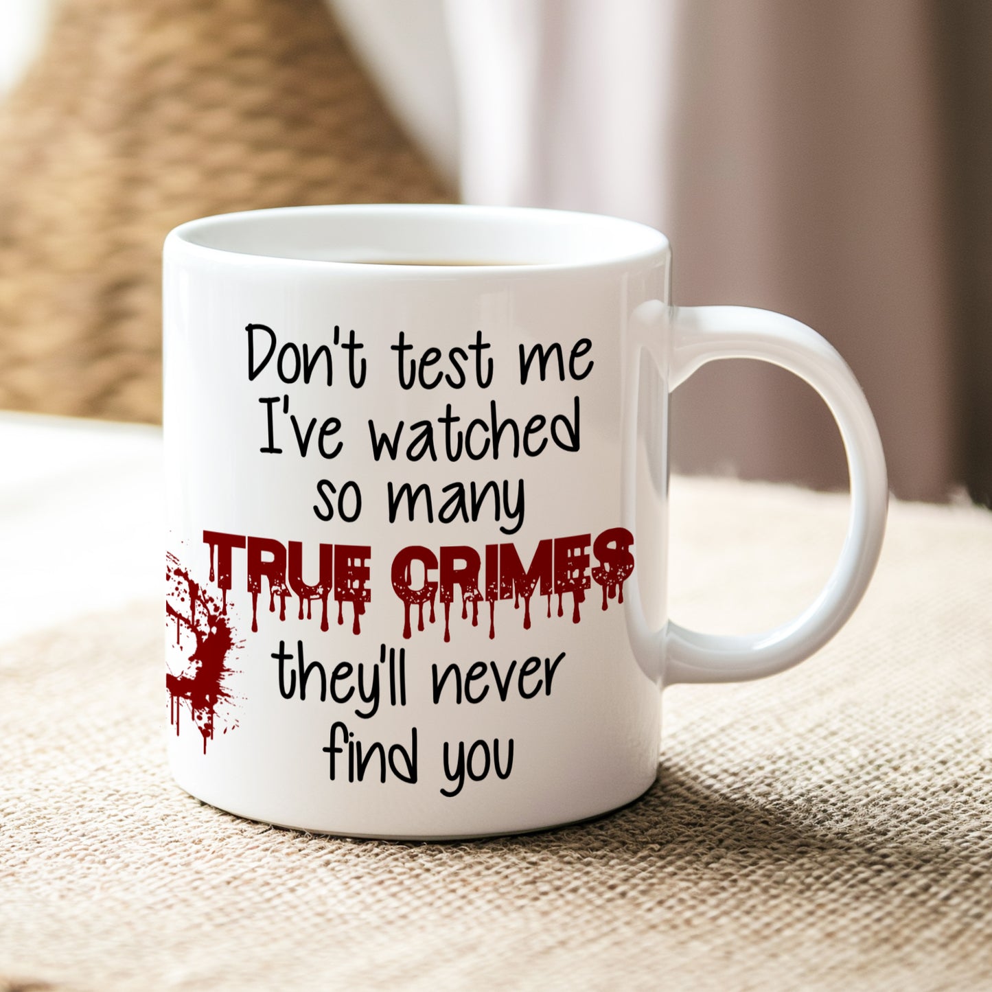 White mug with text 'Don't test me I've watched so many true crimes they'll never find you' on a textured surface.