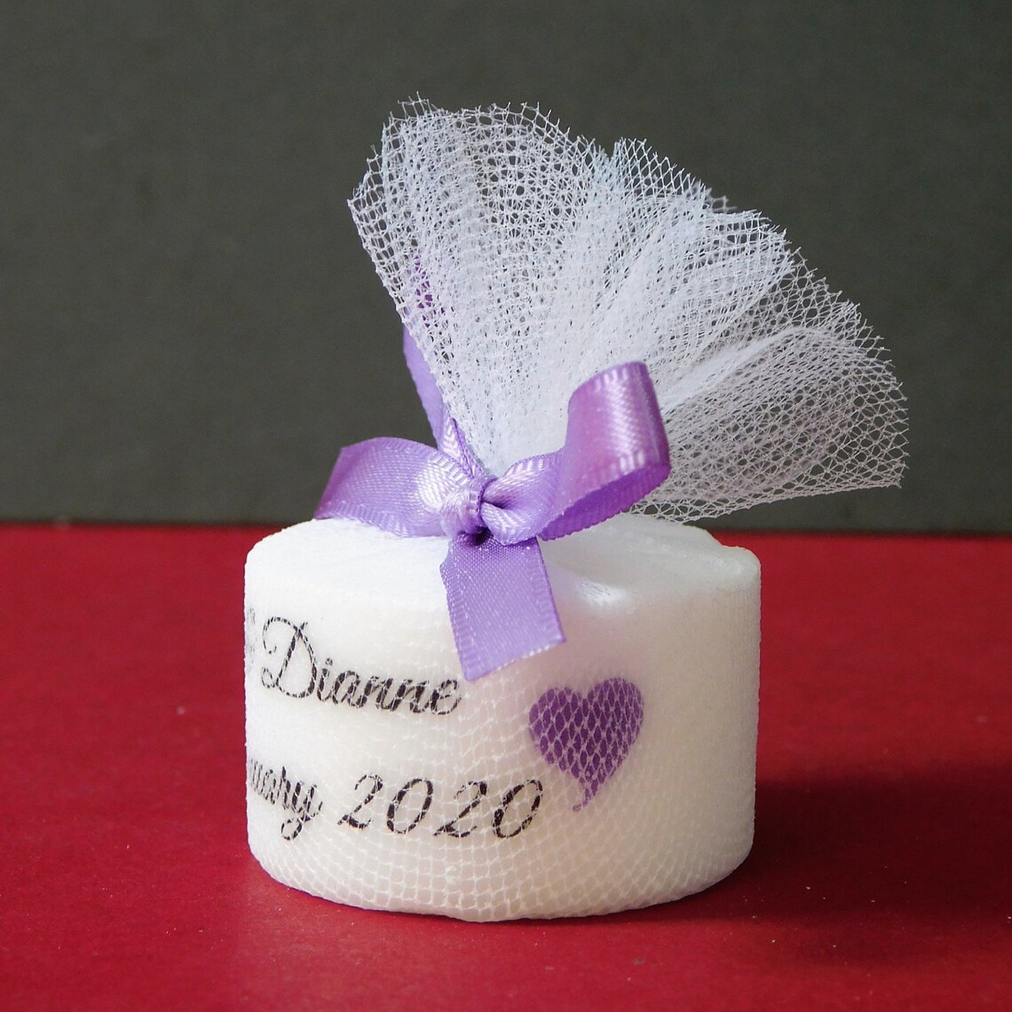 Small white candle with a purple ribbon and mesh on a red surface