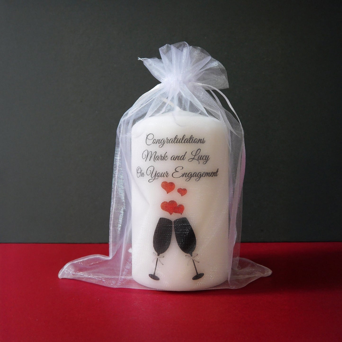 Engagement-themed candle with a祝福message in a clear bag on a red surface.