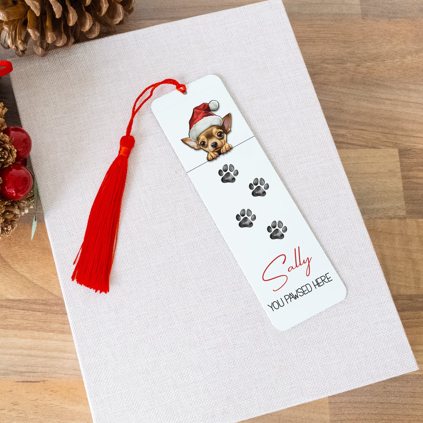 Bookmark with a dog illustration and red tassel on a white card, surrounded by Christmas decorations.