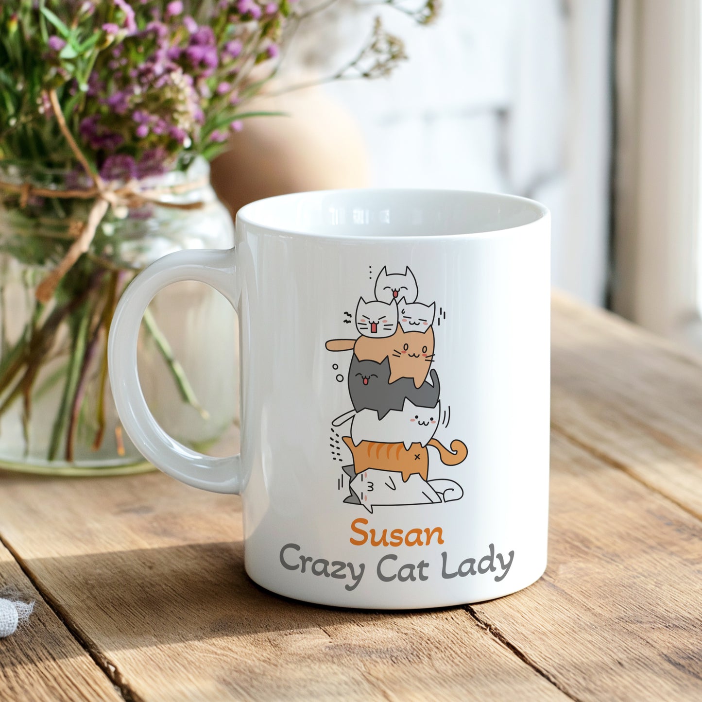 White mug with cat illustration and 'Susan Crazy Cat Lady' text on a wooden table with flowers in the background