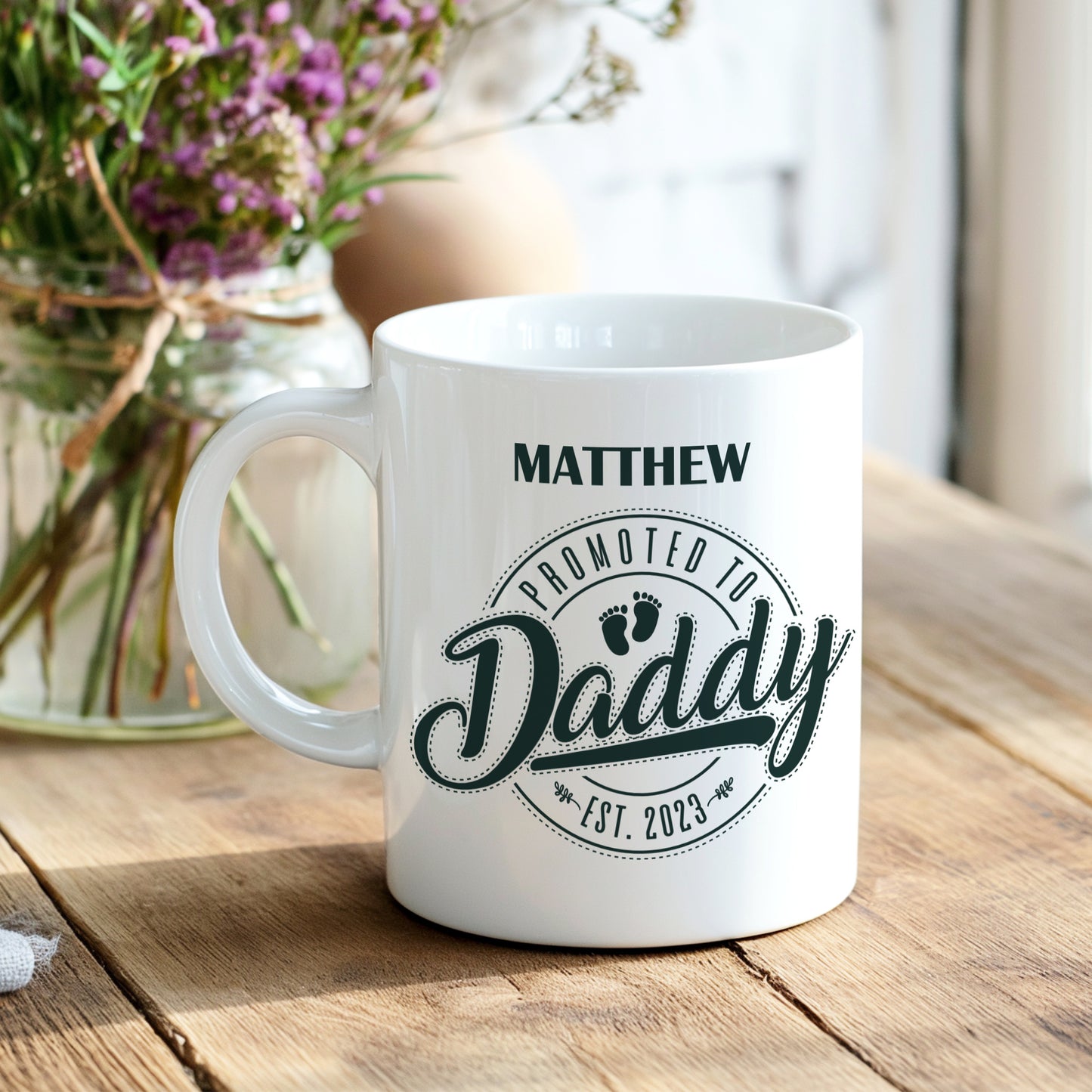 White mug with 'Promoted to Daddy' text on a wooden table with flowers in the background