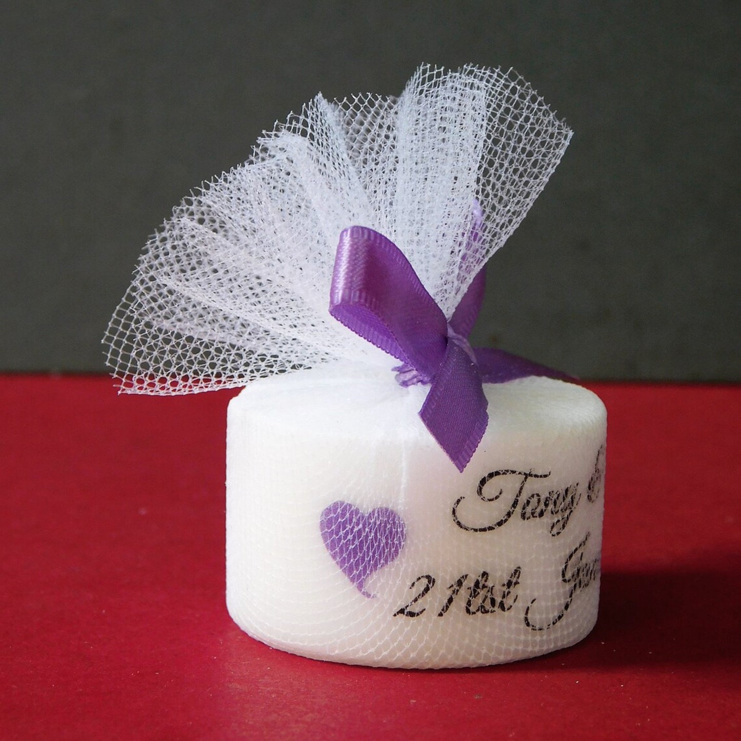 Small white candle with purple ribbon and heart on a red surface