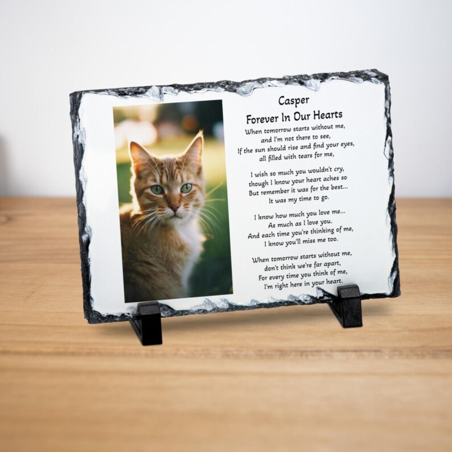 A personalised memorial slate plaque on a small black stand, featuring a photo of an orange tabby cat and the text 'Casper Forever In Our Hearts' with a poem. The plaque is displayed on a light wooden surface against a white background.