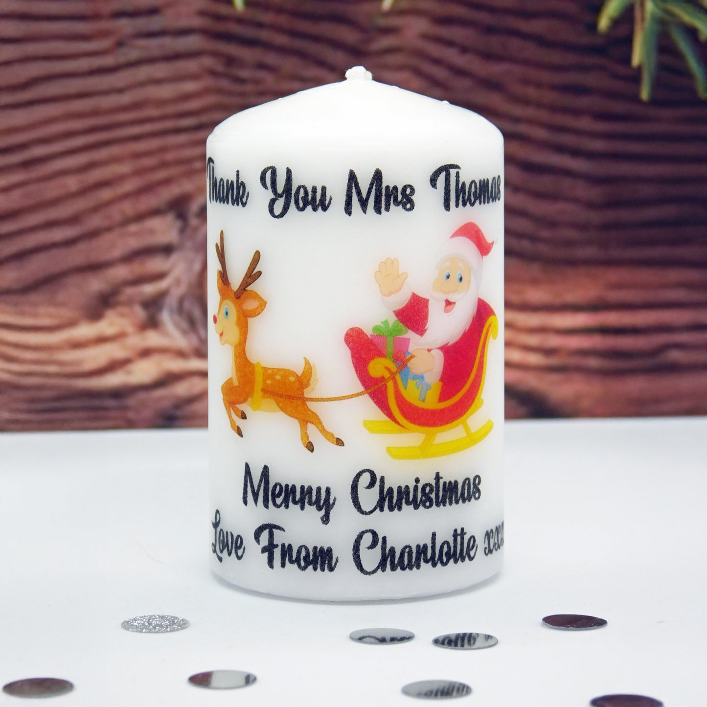 Personalized Christmas candle with Santa Claus and reindeer design, against a wooden background.