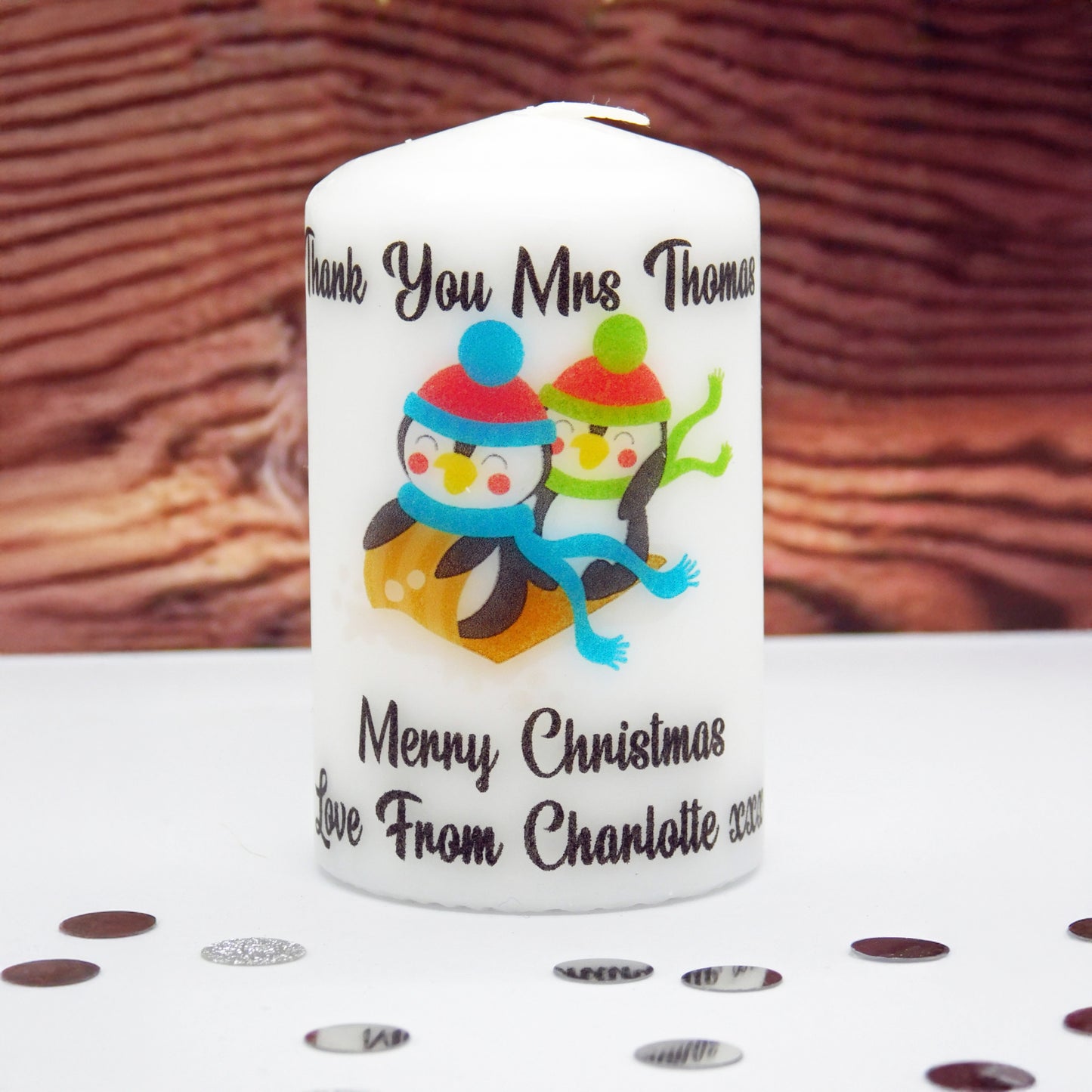 Personalized candle with penguins and text on a wooden surface