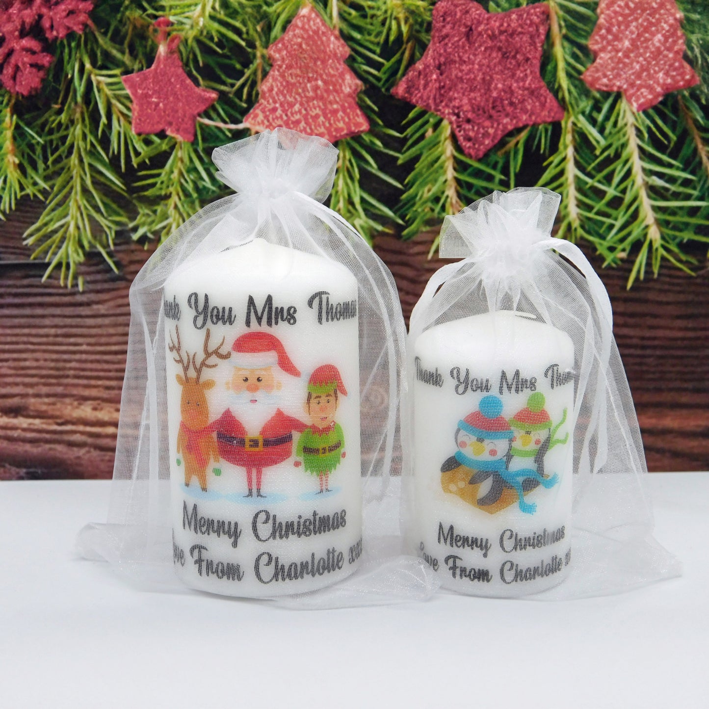 Two Christmas-themed candles in gift bags with festive decorations in the background.