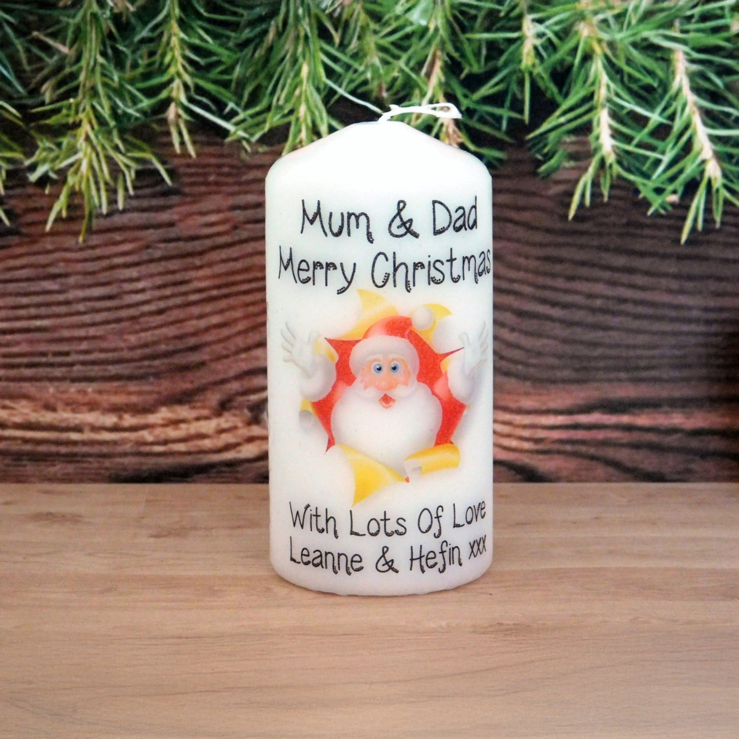 Personalized Christmas candle with Santa Claus design on a wooden surface with greenery in the background.