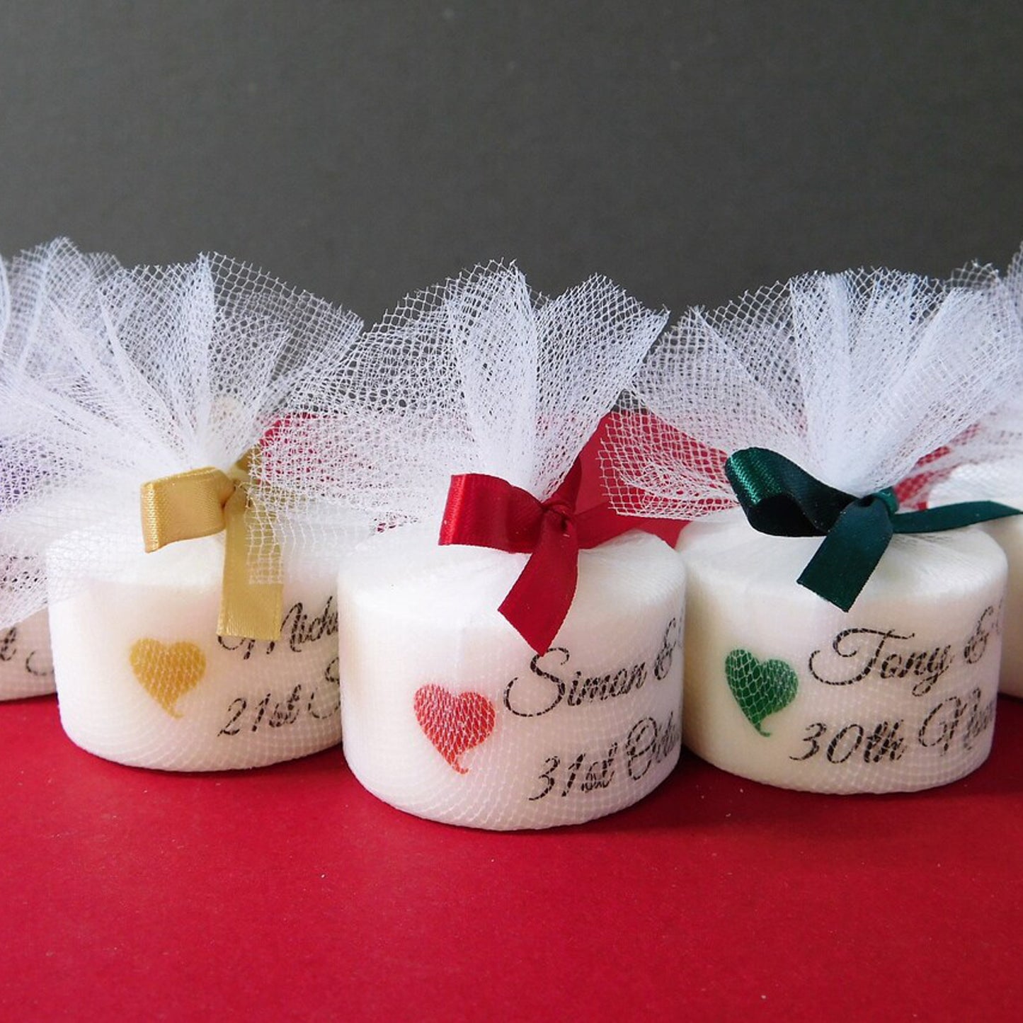 Three small candles with decorative ribbons and personalised text on a red surface.