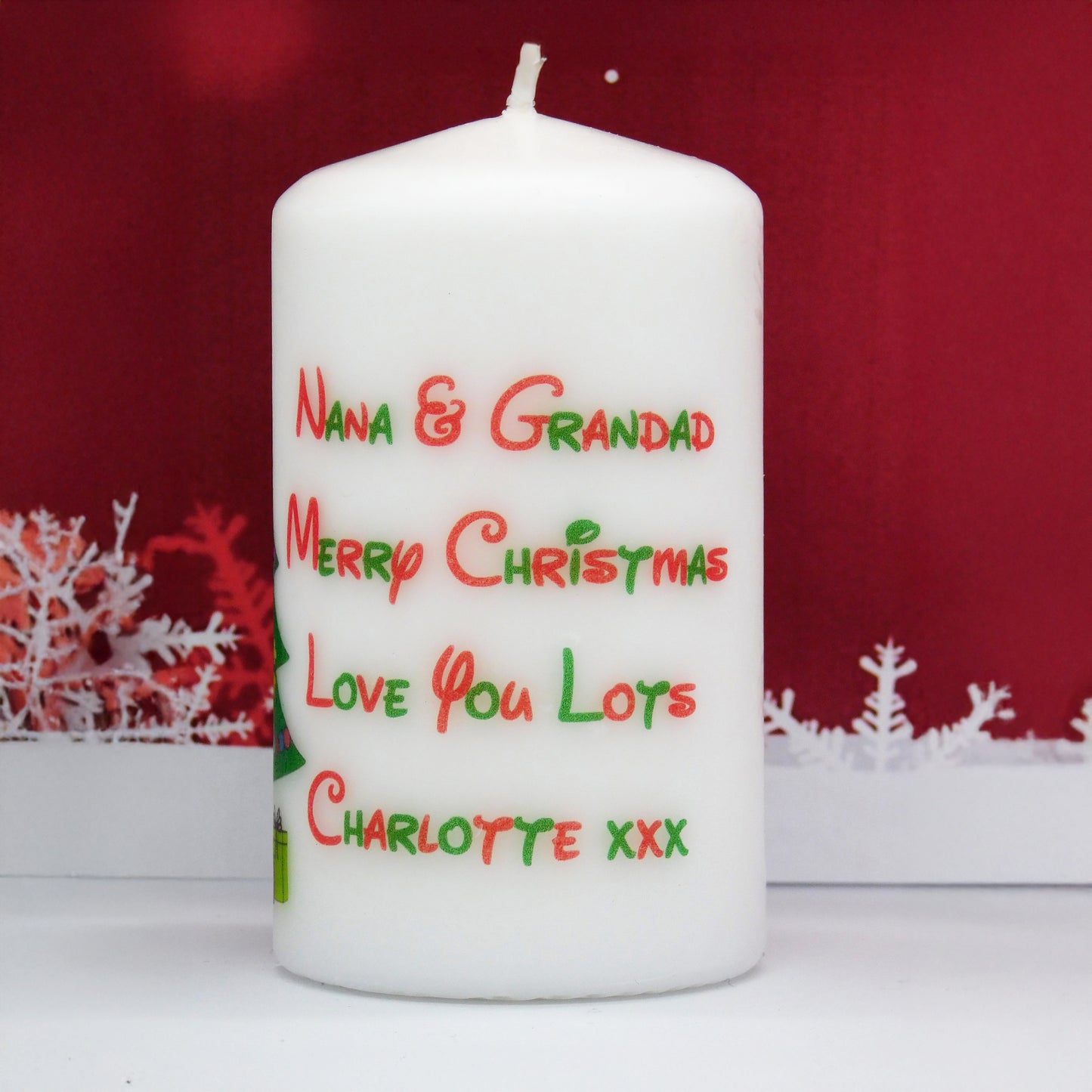White candle with Christmas-themed text on a red background