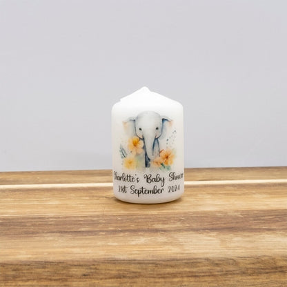 A personalised white pillar candle with a painted elephant and yellow flowers, sitting on a wooden surface against a neutral grey background.