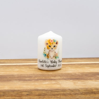 A small white pillar candle with a watercolour cheetah illustration and personalized text reading 'Charlotte's Baby Shower 21st September 2023', displayed on a wooden surface against a light grey background.