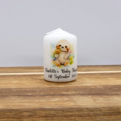 A white house-shaped candle with a watercolour sloth illustration and personalised text reading 'Charlotte's Baby Shower 21st September 2024', displayed on a wooden surface against a neutral grey background.