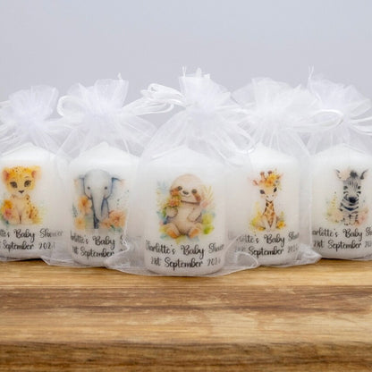 Five personalised baby shower favour candles in clear tulle bags, decorated with watercolour animal illustrations including a lion, elephant, dog, giraffe, and zebra, arranged on a wooden surface against a light grey background.