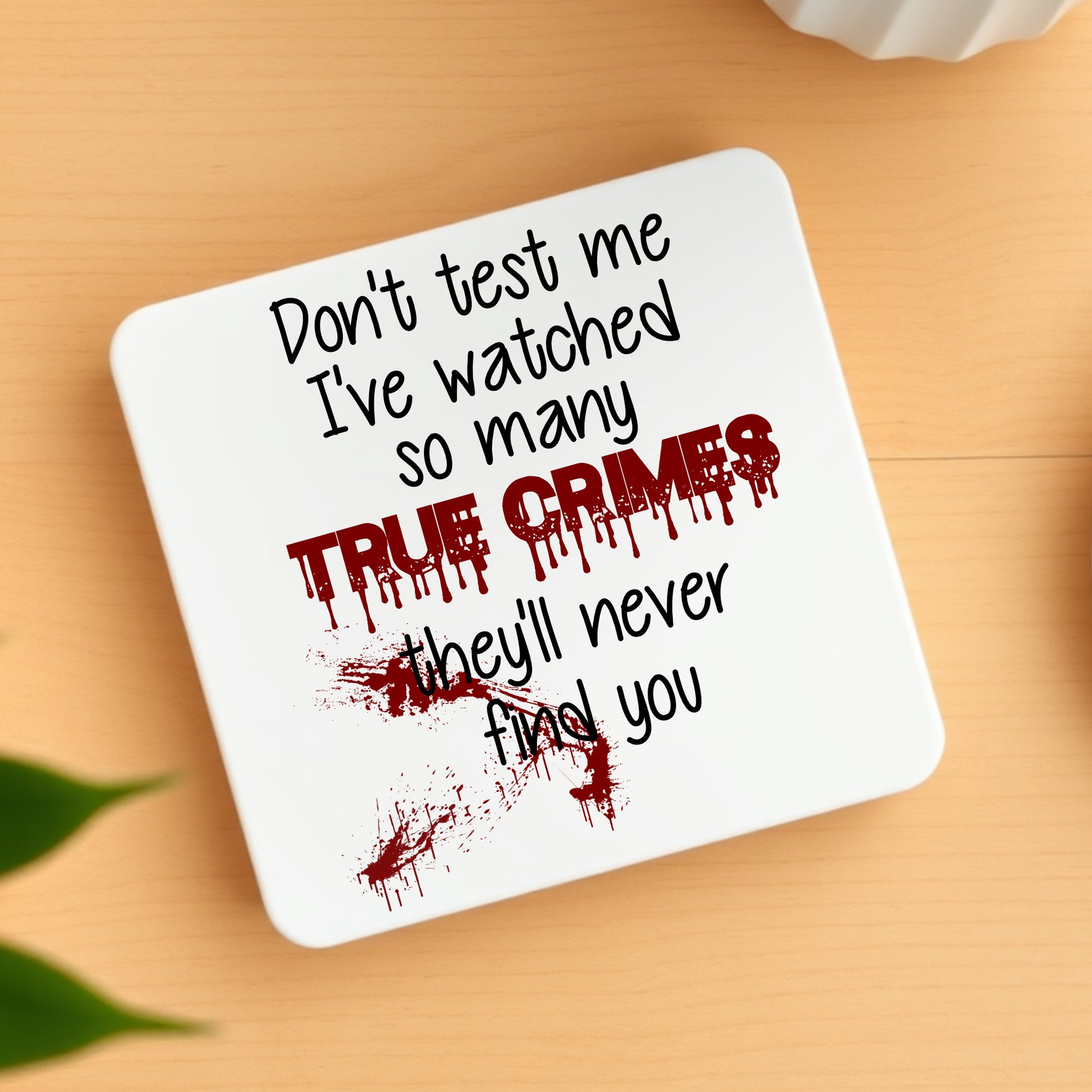 Coaster with text 'Don't test me I've watched so many True Crimes they'll never find you' on a wooden surface.