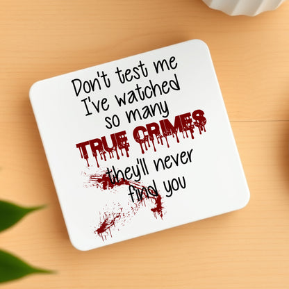 Coaster with text 'Don't test me I've watched so many True Crimes they'll never find you' on a wooden surface.