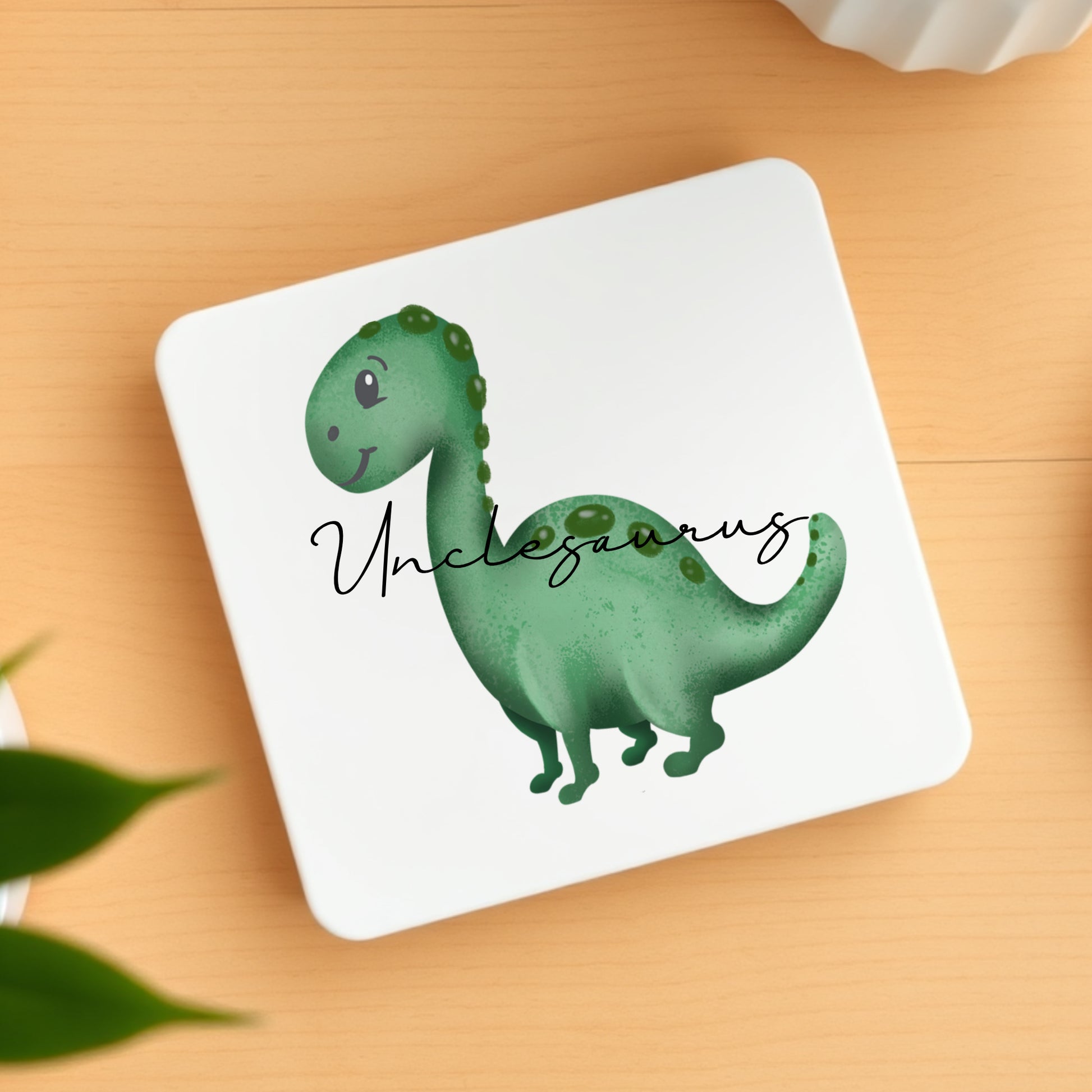 Coaster with a green dinosaur illustration and 'Unclesaurus' text on a wooden surface.