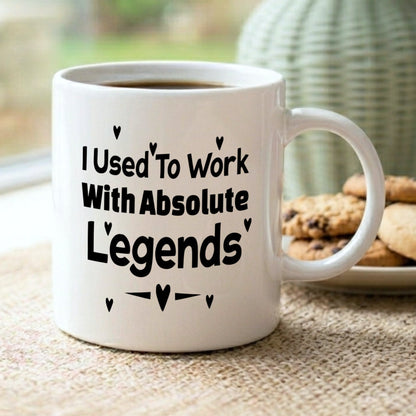 I Used To Work With Absolute Legends' white ceramic mug filled with coffee, displayed on a jute mat on a windowsill with cookies and a sage green vase