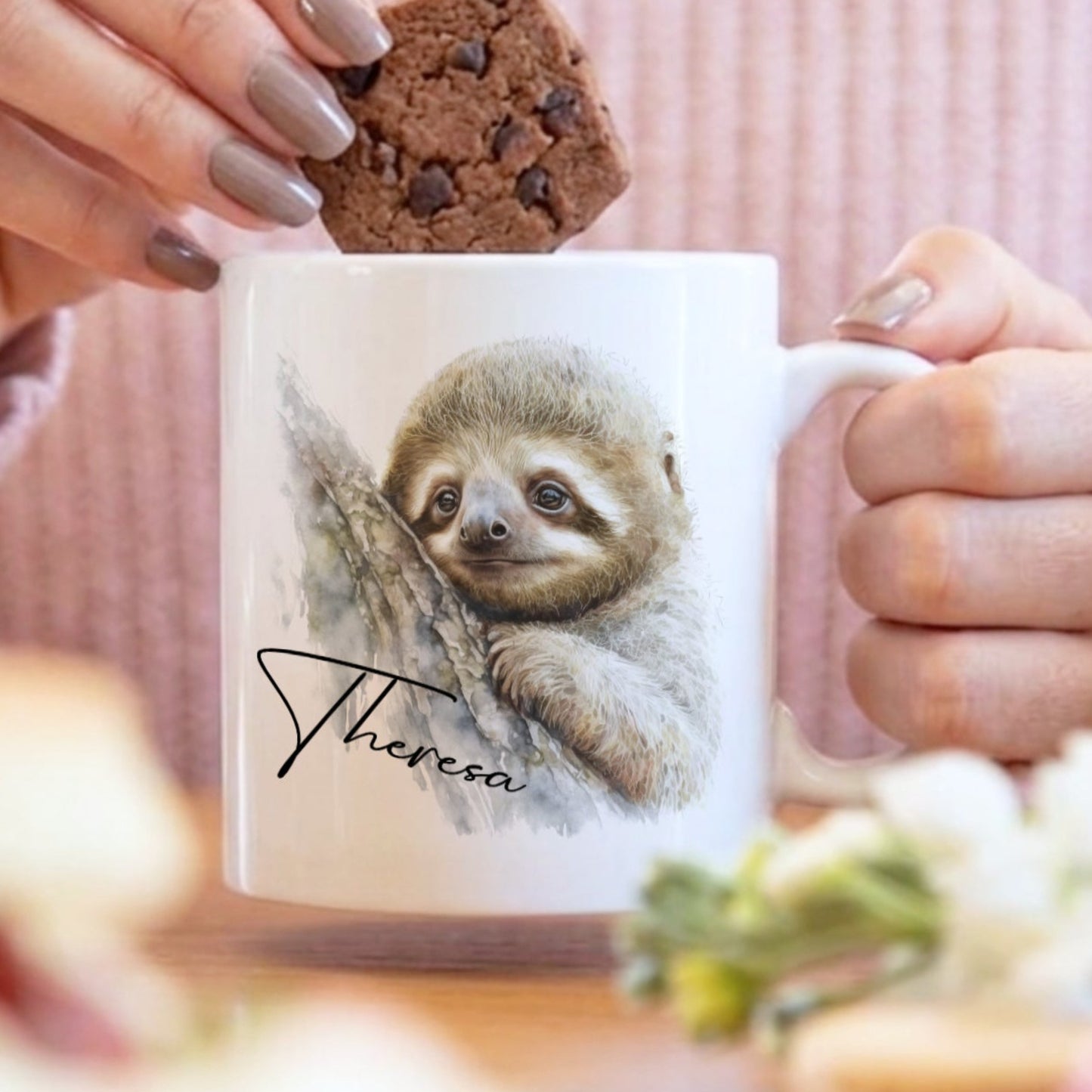 Person holding a mug with a sloth design, eating a cookie.