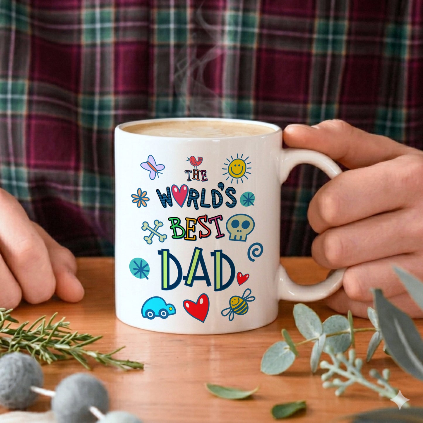 Person holding a mug with 'The World's Best Dad' text and colorful graphics on a wooden table.