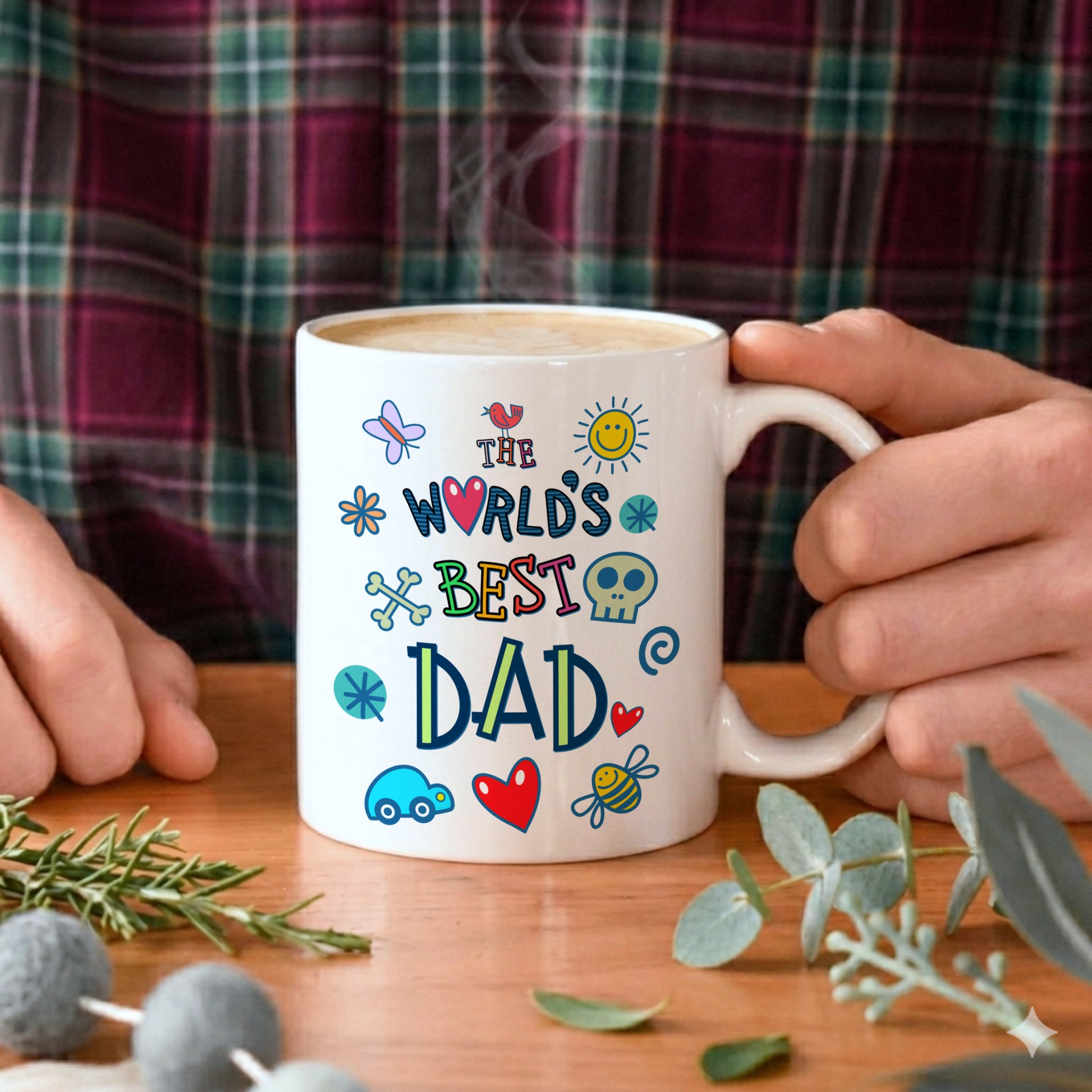 Person holding a mug with 'The World's Best Dad' text and colorful graphics on a wooden table.