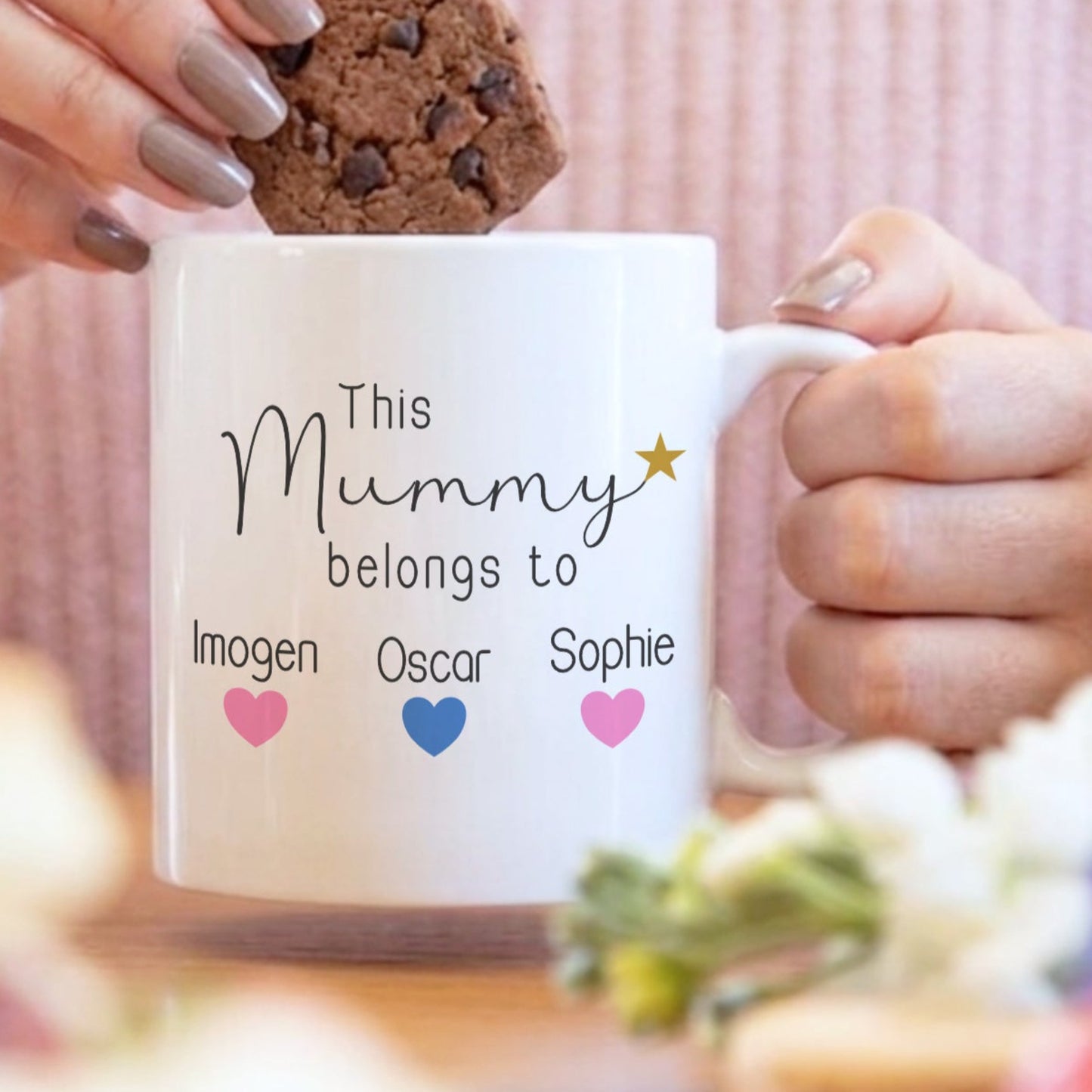 Person holding a mug labeled 'Sarah Bride to be' with a cookie, blurred background