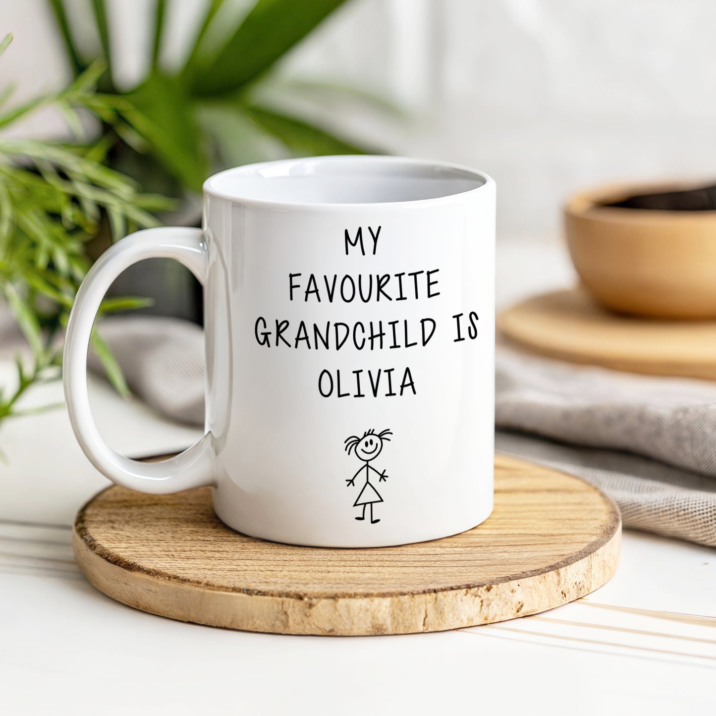 A white mug with my favourite grandchild is Olivia text on a wooden coaster with a blurred background