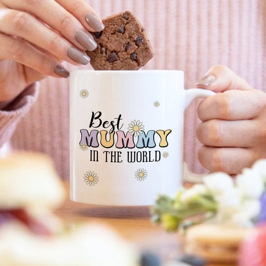 Person holding a mug with 'Best Mummy in the World' text, eating a cookie.
