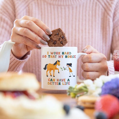 Person holding a mug with a horse-themed design and a cookie, with a blurred background.