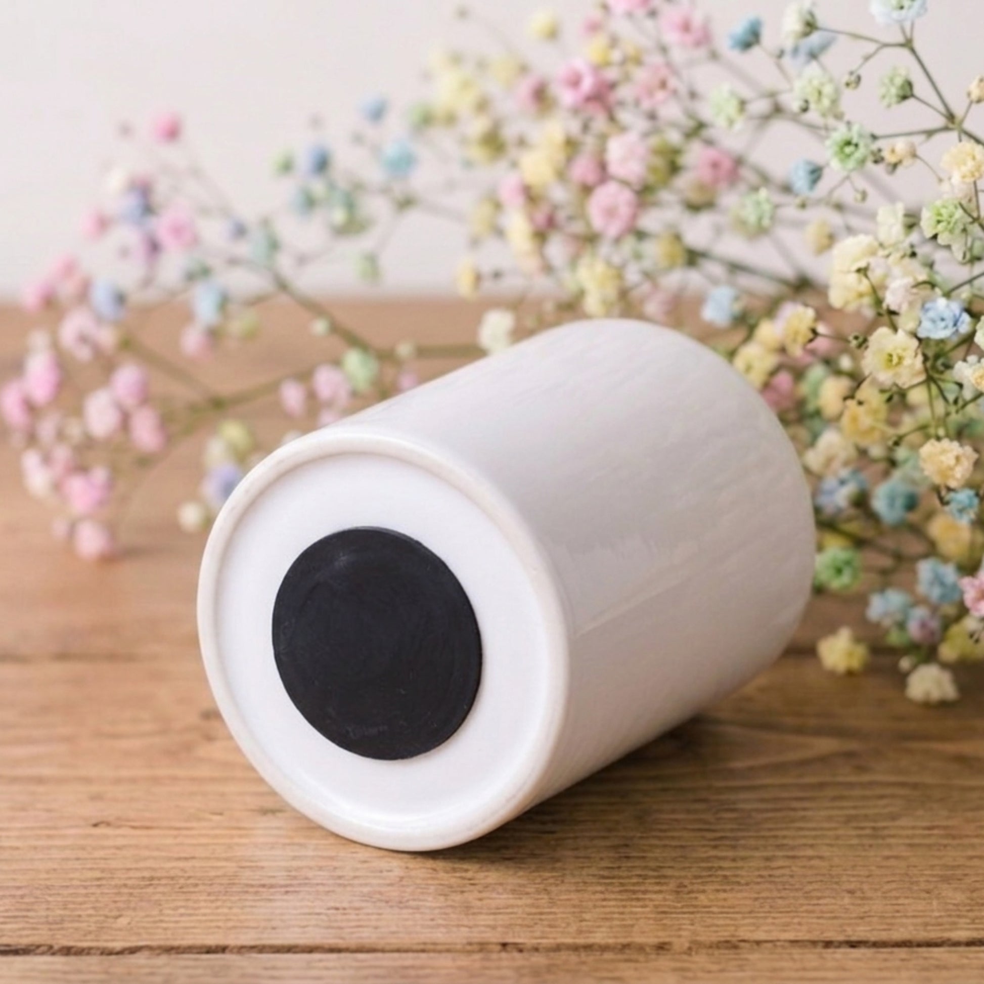White cylindrical object with black center on a wooden surface with flowers in the background
