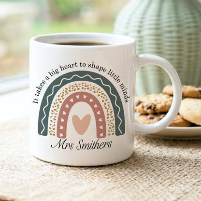 White mug with rainbow design and text on a table with cookies and a vase in the background