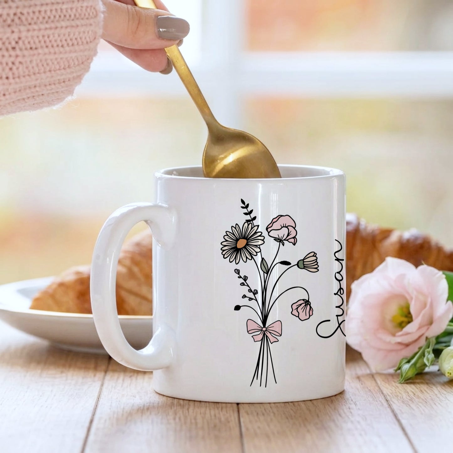 Person holding a mug with floral design and 'Jessica' text, eating a cookie.