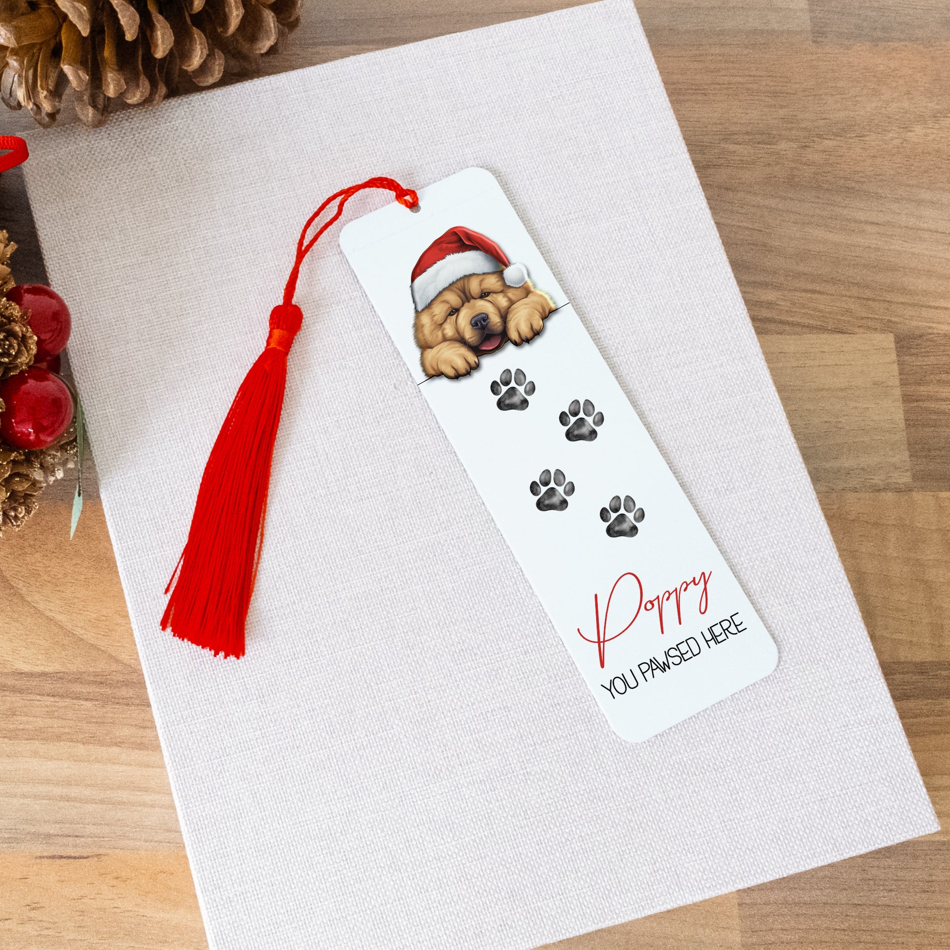 Bookmark with a dog design and tassel on a white card, surrounded by decorative items on a wooden surface.