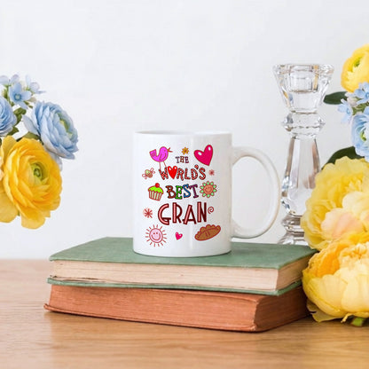 White mug with colorful text on a stack of books surrounded by flowers and a candle.