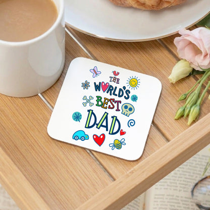Coaster with 'The World's Best Dad' text on a wooden table with a mug and flowers.