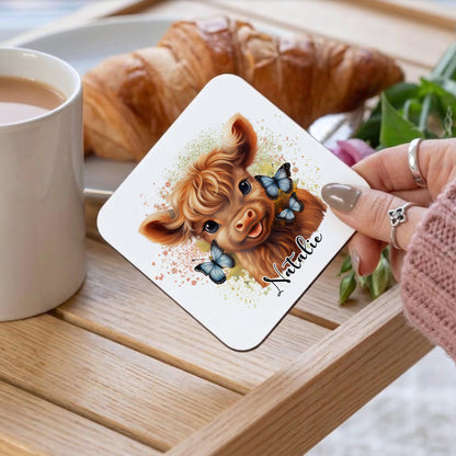 Coaster with a cartoon dog design and name 'Natalie' on a wooden table with a cup of coffee and croissant.