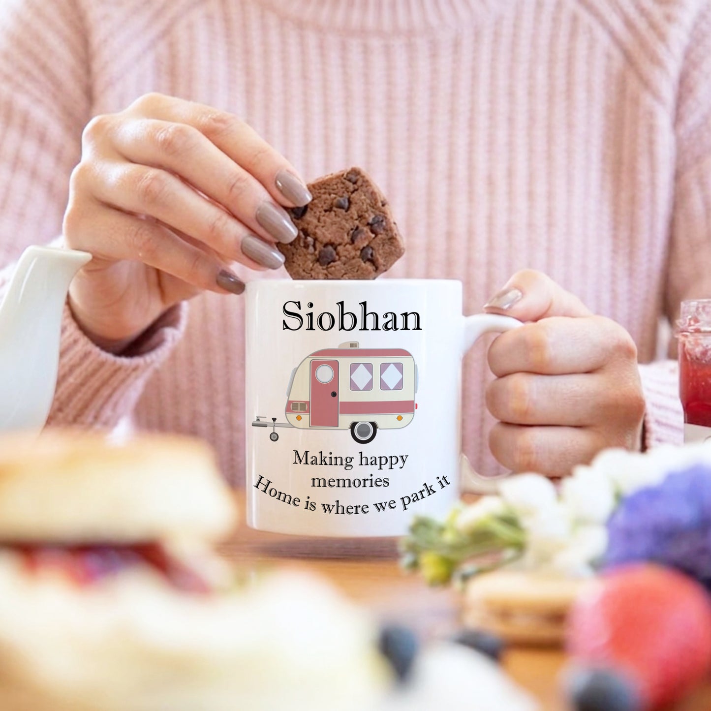 Person holding a mug with 'Siobhan' and caravan design, eating a cookie.